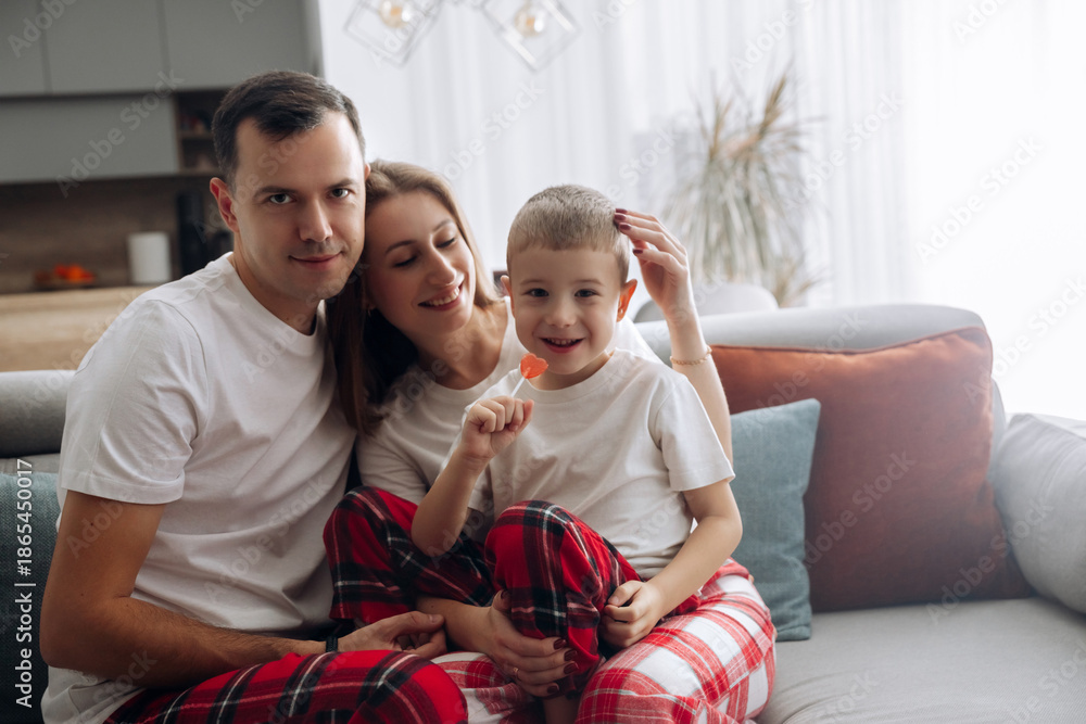Fototapeta premium Family enjoys a cozy moment together on a sofa while wearing matching outfits and sharing smiles in a living room with soft lighting