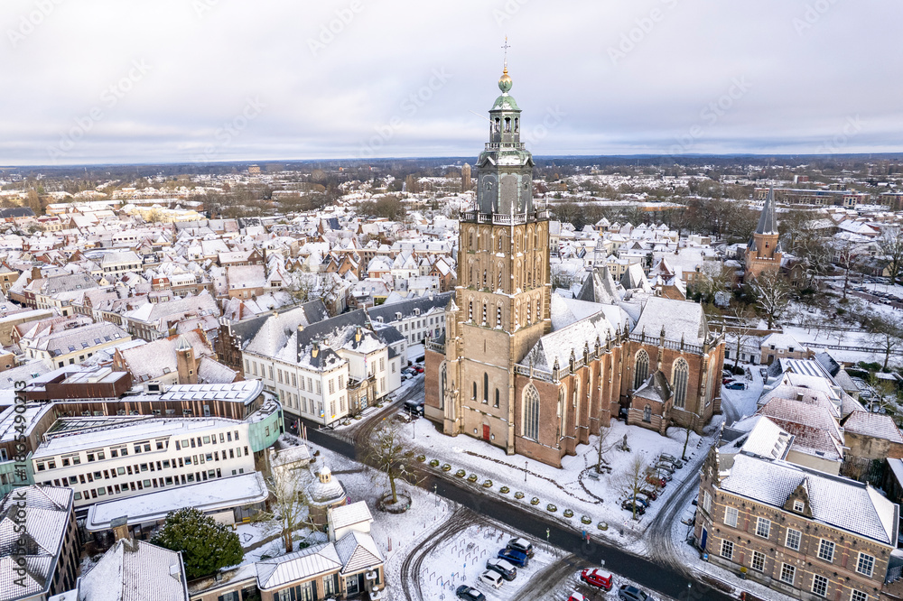 Naklejka premium Warm sunlight on medieval Hanseatic Dutch tower town Zutphen in the Netherlands covered in snow with historic heritage buildings and river IJssel passing by in the background behind Walburgiskerk chur