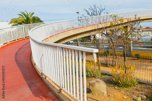 Quadro em tela Curving elevated pedestrian walkway with red surface and metal railings, leading over highway