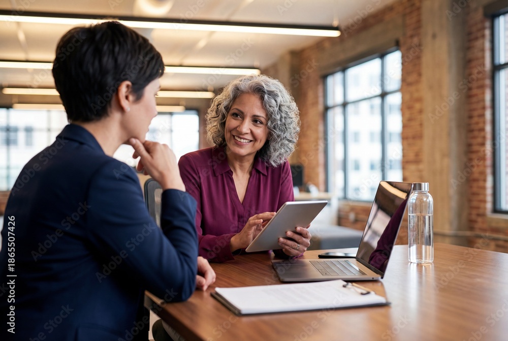 Fototapeta premium Smiling senior manager talking to female colleague with digital tablet in modern brick office