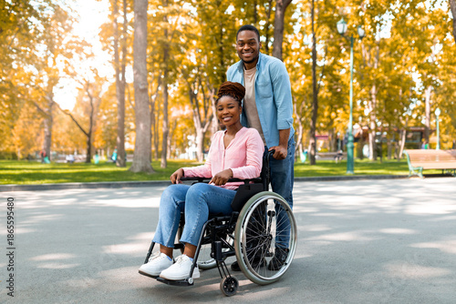 Wallpaper Mural Full length of cheerful black guy taking his impaired girlfriend in wheelchair for walk at city park in autumn. African American disabled couple enjoying fall nature together, outdoors Torontodigital.ca