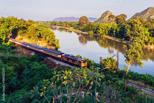 Train Journey along River Kwai. Scenic view of train traversing famous historic curve of Railway line surrounded by green hills at Tham Khao Pun Temple viewpoint. World War II Heritage Rail, Thailand.
