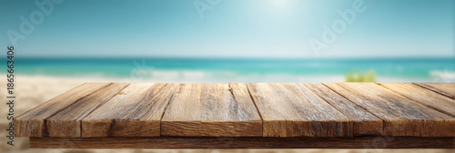 Empty wooden table top with visible natural grain and texture overlooking a blurred sandy beach with turquoise sea and sky in the background