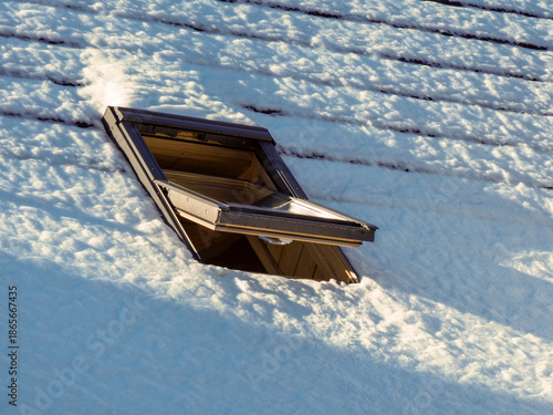 Close up of an open skylight window on a snowy roof in winter