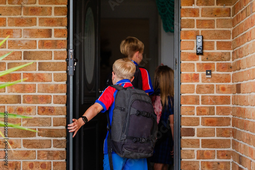 Primary aged children coming home from school walking through front door at home
