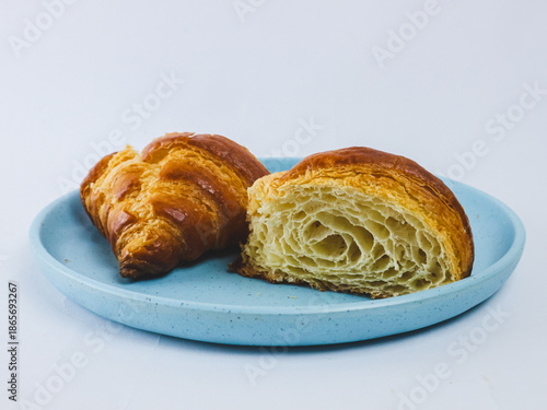 Fresh buttery croissant on a blue ceramic plate, one cut open showing flaky layered crumb, isolated on white background. Minimal bakery food concept with copy space