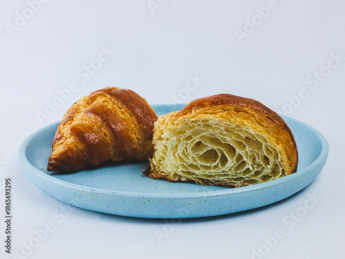 Fresh buttery croissant on a blue ceramic plate, one cut open showing flaky layered crumb, isolated on white background. Minimal bakery food concept with copy space