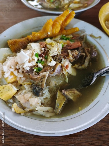 A bowl of soup with various ingredients and a spoon on a wooden table