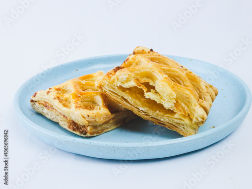 Golden flaky puff pastry cut in half on a blue ceramic plate, showing layered buttery texture, isolated on white background. Minimal bakery food concept with copy space