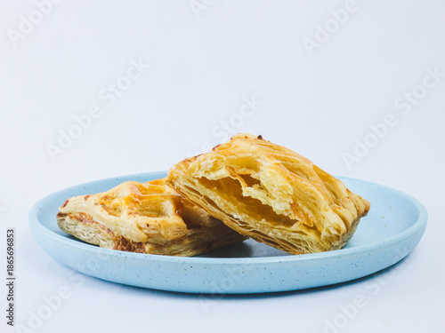 Golden flaky puff pastry cut in half on a blue ceramic plate, showing layered buttery texture, isolated on white background. Minimal bakery food concept with copy space