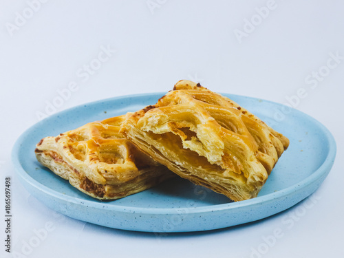 Golden flaky puff pastry cut in half on a blue ceramic plate, showing layered buttery texture, isolated on white background. Minimal bakery food concept with copy space