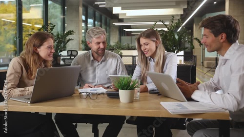 Group of confident business people in smart casual wear working together while sitting at the desk in office