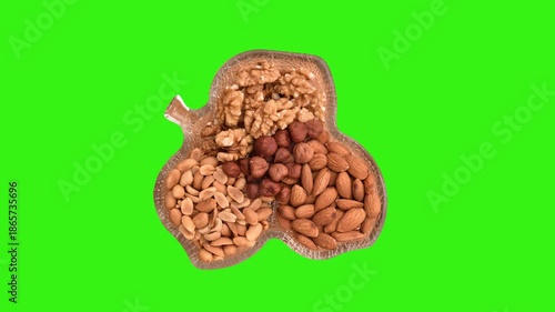 Different types of nuts in leaf-shaped glass bowl rotating on the green screen. Top view. 