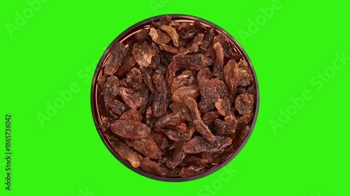 Raisins in decorative glass bowl rotating on the green screen. Top view.