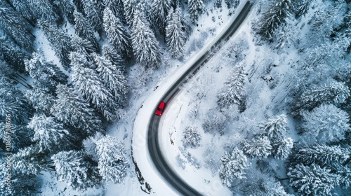 Aerial view of a winding road in a snow-covered forest, with a red car visible