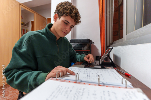 Photos Young student learning and studying at desk, concentrating on homework with note