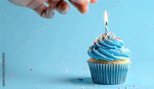 Close Up of a Hand Lighting a Single Candle on a Blue Frosted Cupcake with Sprinkles on a Light Blue Background