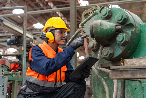 Confident engineer man with safety helmet standing analyzing with tablet in factory warehouse. Asian technician factory inspection and control machinery in industry factory.