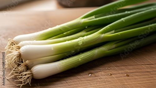 Fresh green onions with white roots on a wooden cutting board, bunch of raw scallions with water droplets for healthy cooking ingredients.