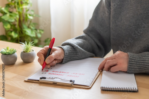 фотографія Person's hand holding a red pen, ticking off items on a checklist titled do list