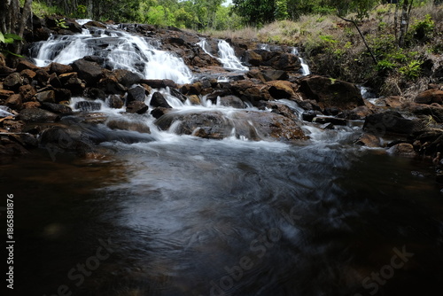 beautiful waterfall with trees and coral. water flows over dark, rugged stones, rocks creating staircase effect. The scene is serene natural landscape.