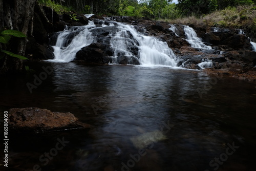 beautiful waterfall with trees and coral. water flows over dark, rugged stones, rocks creating staircase effect. The scene is serene natural landscape.