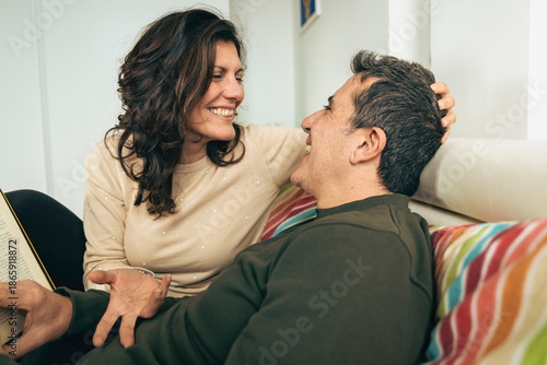Tableau sur toile Happy mature couple laughing together in bed while reading a book, intimate life