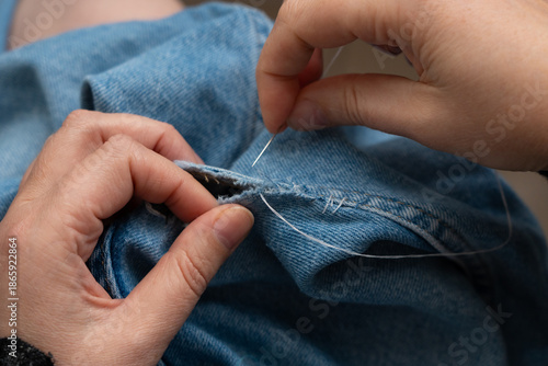 Photos Woman mends jeans by hand with needle
