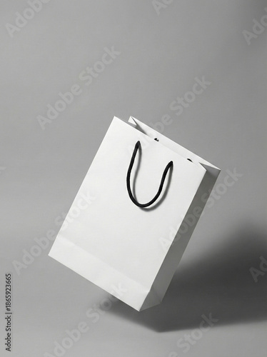 Minimalist white paper shopping bag with black handles floating in mid-air against a grey background.