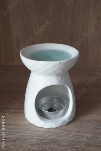 Foto White ceramic oil burner with tealight candle and blue water on a wooden surface