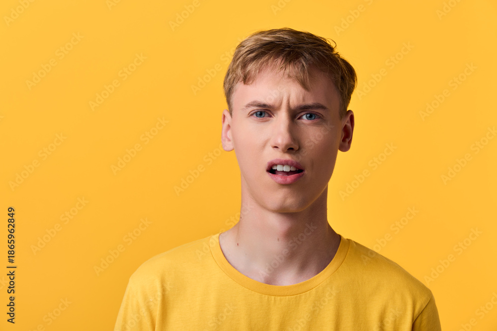 Fototapeta premium Young man in yellow shirt with puzzled expression against a bright yellow backdrop, conveying confusion, uncertainty, or questioning emotions in a studio setting.