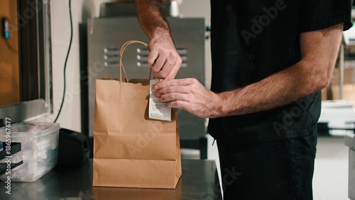 Chef preparing food delivery order, attaching receipt to a takeout paper bag