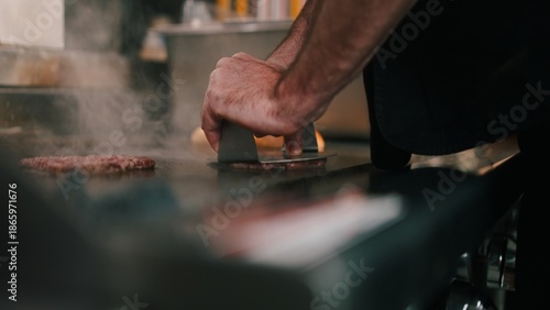 Fotografi Chef smashing ground beef patty on a hot griddle in a dark commercial kitchen