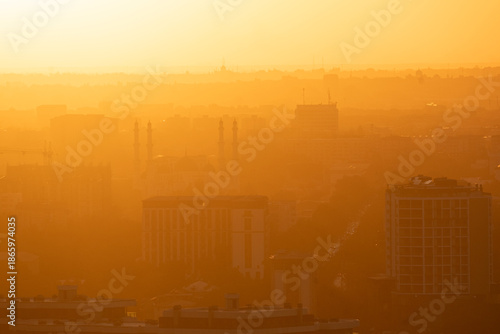 The scene captures a city skyline at sunset. Buildings appear silhouetted against a bright orange and yellow sky. Tashkent, Uzbekistan 09/10/2025