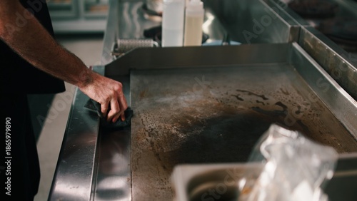 Foto Chef cleaning a flat top griddle in a dark commercial kitchen for food preparati