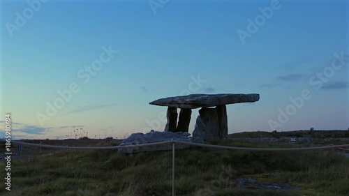Aerial orbit of Poulnabrone Dolmen with rope barriers in the foreground at twilight under soft evening light. Ireland