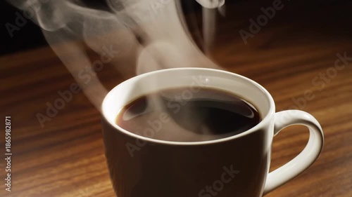 Steaming white mug filled with hot dark coffee rests on a textured wooden surface, emitting wisps of aromatic steam.