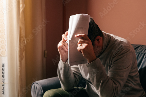 Fotografía Stressed man overwhelmed by paperwork while working on the couch at home