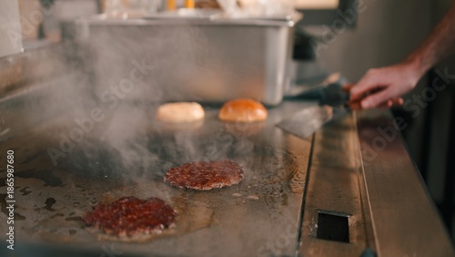 Tableau sur toile Chef cooking burger patties on flat top grill during busy dark kitchen workflow