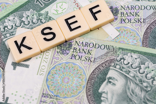 Blocks with the abbreviation KSEF, standing for National E-invoice System, are placed against a background of loosely spread Polish 100 PLN banknotes. The photo was taken under artificial lighting.