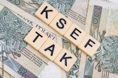 Blocks with the abbreviation TAK KSEF, standing for positives about National E-invoice System, are placed against a background of loosely spread Polish 100 PLN banknotes. 