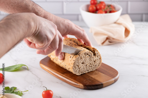 Photos Man's hands slicing fresh whole grain bread on a wooden board, on marble countertop
