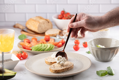 Slika na platnu Male hand adding fresh cheese to whole grain toasts on ceramic plate