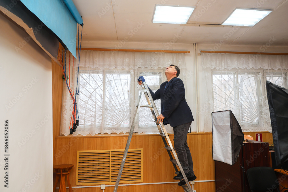 Fototapeta premium Man on Step Ladder in Photo Studio Checking Ceiling Light Fixture.