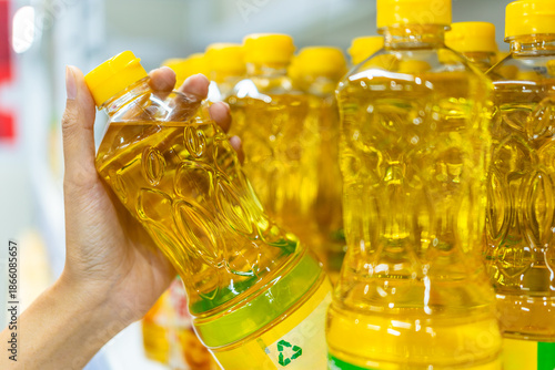 Close up asian woman selects bottled sunflower oil for home cooking from a shelf in a supermarket. Shopping concept