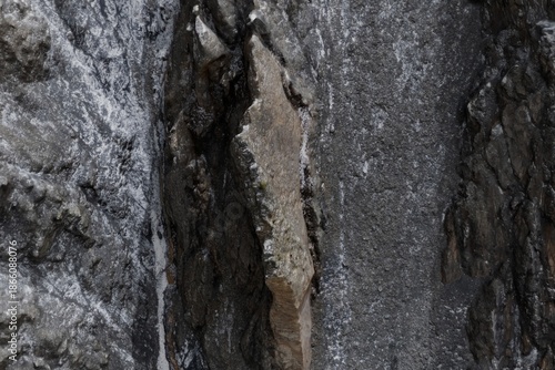 Fotografi Textured dark rock walls with ice, framing a prominent lighter, angular rock slab