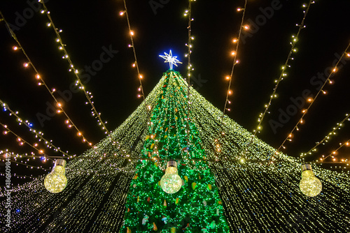 Bright christmas tree lights with glowing bulb in foreground and star on top creating magical festive holiday mood at night