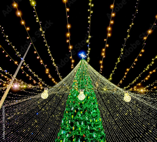 Bright christmas tree lights with glowing bulb in foreground and star on top creating magical festive holiday mood at night