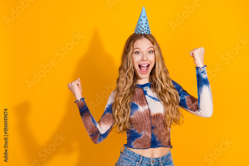 Young woman celebrates birthday with party hat and tie dye top against yellow background