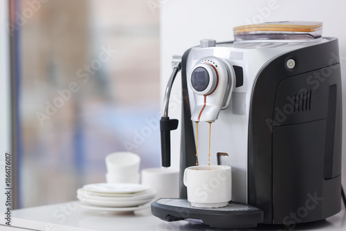 Electric espresso machine making coffee, plates and cups on white table indoors, closeup. Space for text
